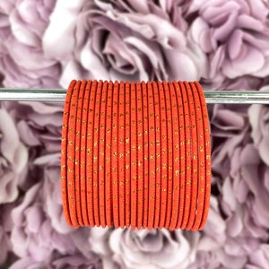 May include: A stack of 20 orange bangles with gold glitter. The bangles are arranged in a circle and are on a silver metal rod.