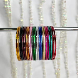 Op de afbeelding: Een set van 18 kleurrijke metalen armbanden, gestapeld en gerangschikt in een regenboogpatroon. De armbanden zijn glanzend en hebben een metallic afwerking.