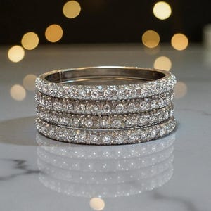 May include: Five silver bangles, each covered in clear, sparkling gemstones. The bangles are stacked, reflecting light. The jewellery is displayed on a light-coloured surface, with a blurred background.