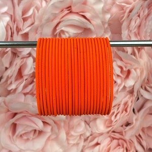 May include: A stack of 20 orange bangles, arranged in a circle, hanging from a silver rod. The bangles are made of a smooth, shiny material.
