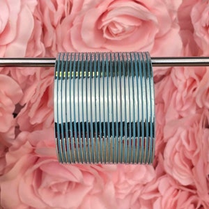 May include: A stack of silver bangles with a light blue stripe around each bangle.