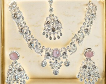 Könnte beinhalten: Ein silberfarbenes Schmuckset mit Halskette, Ohrringen und einem Kopfschmuck, alle verziert mit klaren und rosa Edelsteinen. Das Set wird in einer goldgerahmten Box präsentiert, die die komplizierten Details des Designs hervorhebt.