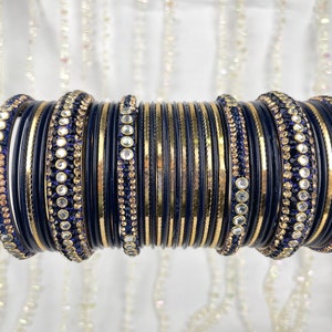 May include: A set of 18 bangles in black and gold with blue rhinestones. The bangles are stacked together and are ready to be worn.