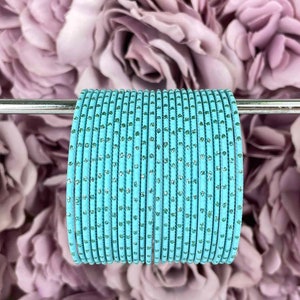 Può includere: Un set di braccialetti di colore azzurro chiaro con punti di glitter argentati. I braccialetti sono disposti su un'asta argentata.