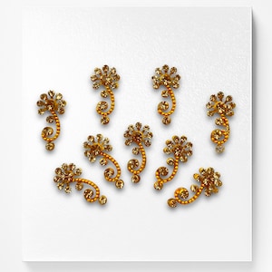 May include: Ten gold-colored, jeweled, floral-shaped stickers with a swirl design.