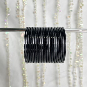 May include: A stack of black bangle bracelets. The bracelets are made of metal and have a shiny finish.