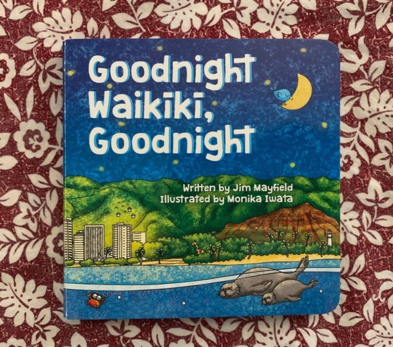 May include: A blue children's book with the title "Goodnight Waikiki, Goodnight". The cover features a cityscape with palm trees, a beach, and a moon with a bird on it. The book is written by Jim Mayfield and illustrated by Monika Iwata.