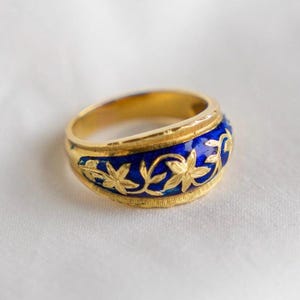 Könnte beinhalten: Ein goldener Ring mit einem blauen Emailleband und einem floralen Design. Das Band ist mit goldenen Blättern und Blumen verziert.