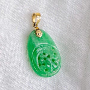 May include: A green jade pendant with intricate carvings, set in a gold bail.