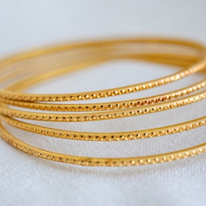 May include: A set of four gold bangles with a textured design. The bangles are stacked on top of each other.