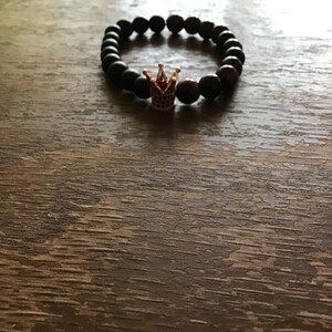 May include: A black beaded bracelet with a gold crown charm.