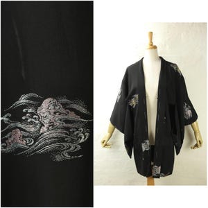 May include: Black kimono with embroidered wave and floral design. The kimono is displayed on a mannequin. The sleeves and lower portion of the kimono feature the embroidered design in shades of pink, silver, and gold.