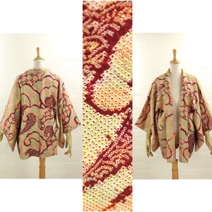 Op de afbeelding: Een vintage kimono-achtige jas in beige, roze en bordeauxrood, gepresenteerd op een mannequin. De jas heeft een gedetailleerd patroon van wervelende vormen en een close-up toont de ingewikkelde stofweefsel. De mouwen zijn wijd en de jas heeft een relaxte pasvorm.