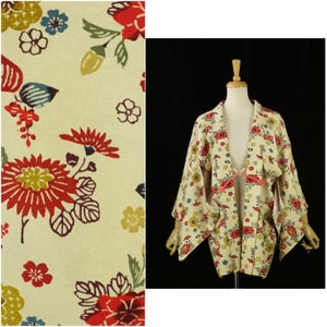 May include: Cream-colored kimono-style jacket with a vibrant floral pattern in red, yellow, blue, and green. The jacket features wide sleeves and a tie closure. The fabric is adorned with large, stylized flower and leaf motifs.