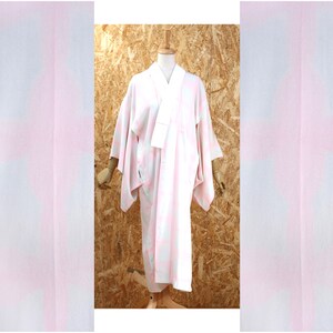 Peut inclure: Un kimono blanc avec un motif dégradé rose et bleu. Le kimono est présenté sur un mannequin sur un fond en bois.