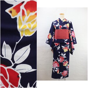 May include: A navy blue yukata, a traditional Japanese garment, featuring a floral pattern of red, yellow, and white flowers. The yukata is cinched with a red obi sash. The fabric is a dark blue with a repeating floral design.