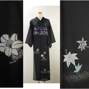 May include: Black kimono with white floral and leaf patterns. The kimono features a blue and gold obi belt. The fabric has a delicate texture. The design includes white and silver accents, creating a striking contrast.