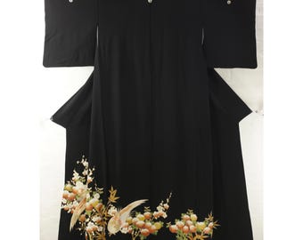May include: A black kimono featuring long sleeves and three white circular crests along the upper back. The lower portion is decorated with an embroidered pattern of golden-toned birds, white and orange flowers, and green bamboo leaves.