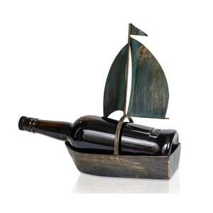 Puede incluir: Un porta botellas de vino de metal con forma de velero con una vela verde y azul. El porta botellas tiene un acabado en bronce r&uacute;stico.