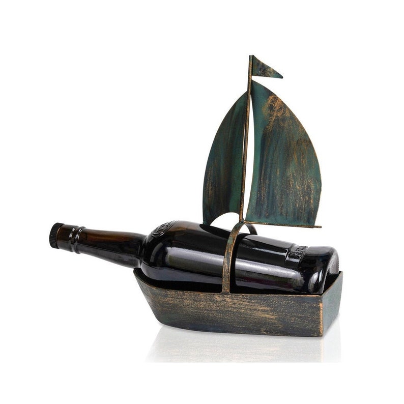 Puede incluir: Un porta botellas de vino de metal con forma de velero con una vela verde y azul. El porta botellas tiene un acabado en bronce r&uacute;stico.