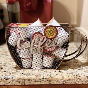 May include: A metal coffee pod holder with a mesh design. The holder is filled with coffee pods and has the word "Coffee" written on it in a decorative font.