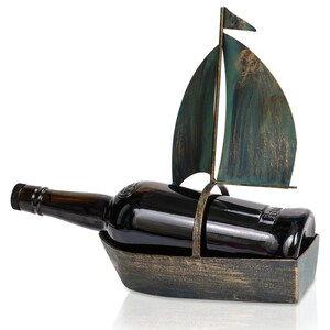 Puede incluir: Un porta botellas de vino de metal con forma de velero con un acabado verde y dorado. El porta botellas est&aacute; sosteniendo una botella de vino de vidrio oscuro.