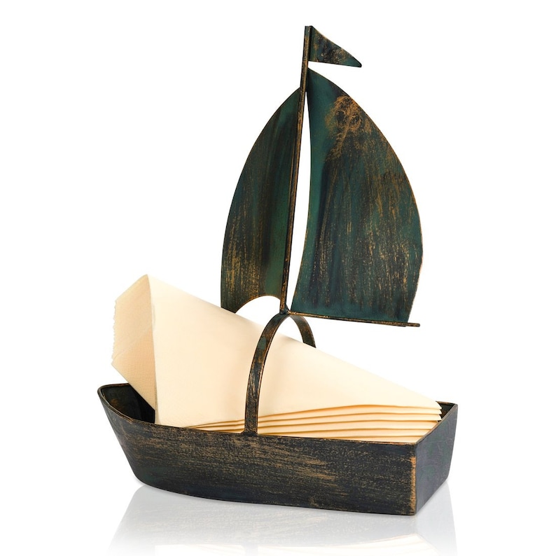 Puede incluir: Un porta servilletas de metal con forma de velero con un acabado verde y marr&oacute;n desgastado. El porta servilletas tiene una vela y un peque&ntilde;o barco con un lugar para sostener las servilletas.