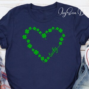 May include: A navy blue t-shirt with a green shamrock heart design and the word "lucky". This St. Patrick's Day themed shirt is a casual wear item.