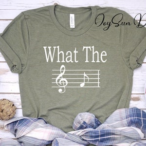 May include: A green t-shirt with the text "What The" and a treble clef and note on a musical staff printed in white.