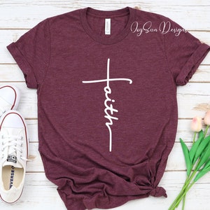 May include: A maroon t-shirt with a white cross and the word "faith" in a script font. The shirt is styled with white sneakers and a bouquet of pink tulips. The text "Joy Sun Designs" is printed in the upper right corner.