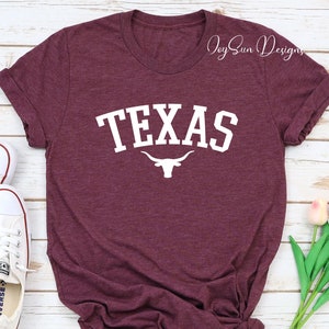 May include: Burgundy t-shirt with white text that says "TEXAS" and a white longhorn steer silhouette.