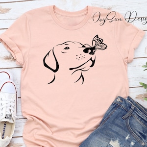 May include: A pink t-shirt with a black silhouette of a dog sniffing a butterfly. The text "Joy Sun Design" is in the top right corner of the shirt.