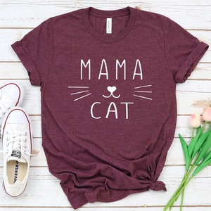 May include: Burgundy t-shirt with white text that reads "Mama Cat" and a stylized cat face with a heart for a nose.