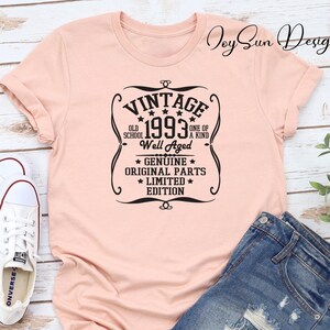 May include: A peach-colored t-shirt with a black vintage-style graphic that says "Vintage 1993 Old School Well Aged Genuine Original Parts Limited Edition".