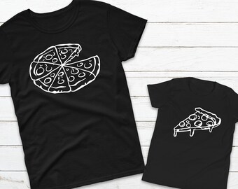May include: Two black t-shirts with white pizza designs. The larger shirt has a whole pizza with a slice missing. The smaller shirt has a single slice of pizza.
