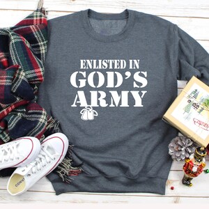 May include: A dark gray sweatshirt with the text "Enlisted in God's Army" in white lettering. The sweatshirt has a white outline of two dog tags.
