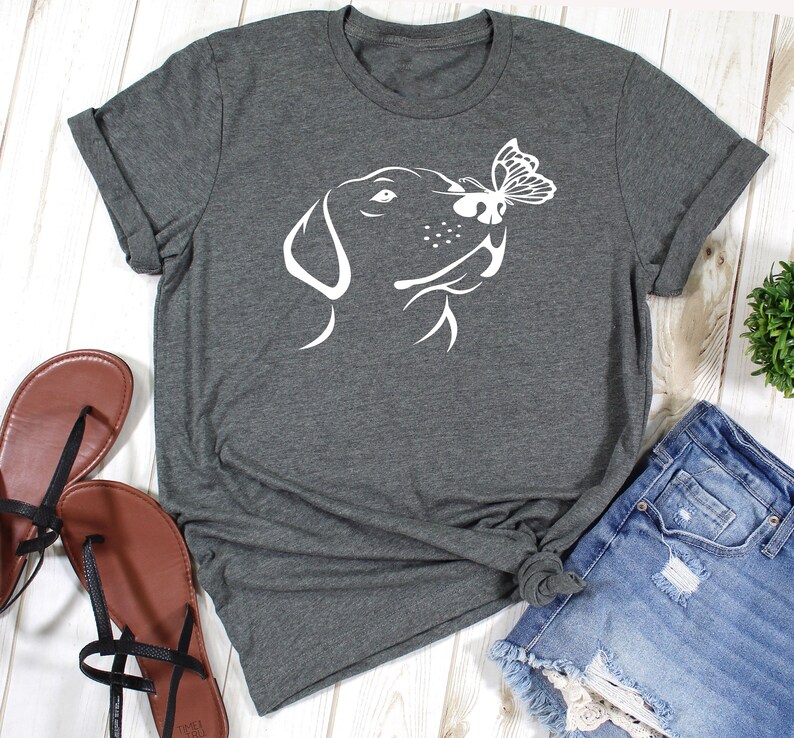 May include: A dark gray t-shirt with a white silhouette of a dog's head sniffing a butterfly. The dog's head is facing the right side of the image.