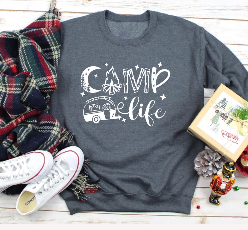 Pu&ograve; includere: Una felpa grigia scura con il testo "Camp life" in bianco. Il design include un fal&ograve;, una luna, stelle e un camper.