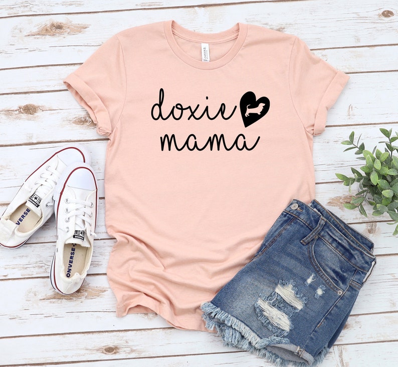 K&ouml;nnte beinhalten: Ein rosa T-Shirt mit dem Text "doxie mama" und einer schwarzen Silhouette eines Dackels in einem Herzen.