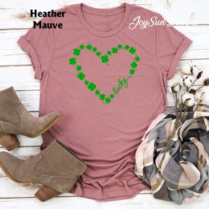 May include: Mauve t-shirt with a green shamrock heart design and the word "lucky". The shirt is a soft, casual style. The image also shows a pair of brown suede boots and a scarf.