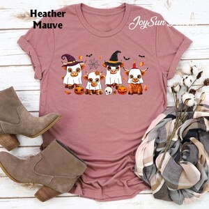 May include: Heather Mauve t-shirt featuring a Halloween-themed graphic. The design includes four cartoon cows dressed in costumes, pumpkins, a spider web, and the text "Joy Sun".