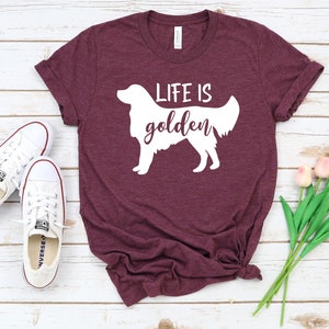 May include: A maroon t-shirt with a white silhouette of a golden retriever and the text "Life is golden".