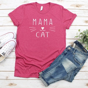 May include: A pink t-shirt with the text "Mama Cat" in white lettering. The text is accompanied by a stylized cat face with a heart for the nose.