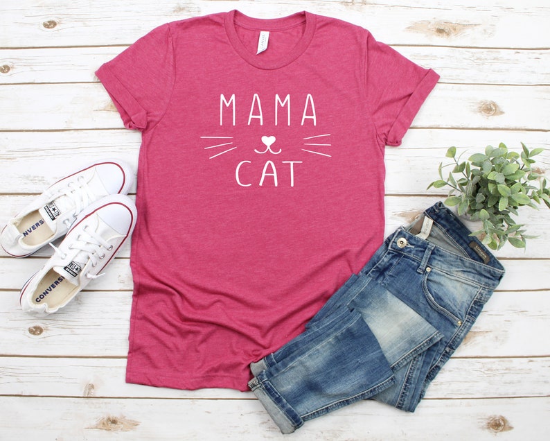 May include: A pink t-shirt with the text "Mama Cat" in white lettering. The text is accompanied by a stylized cat face with a heart for the nose.