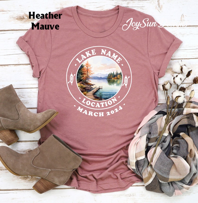 May include: Heather mauve t-shirt with a white circle graphic featuring a lake scene, the text "LAKE NAME", "LOCATION", and "MARCH 2024".