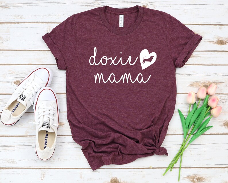 K&ouml;nnte beinhalten: Burgunderfarbenes T-Shirt mit wei&szlig;em Text "doxie mama" und einer wei&szlig;en Silhouette eines Dackels in einem Herzen.