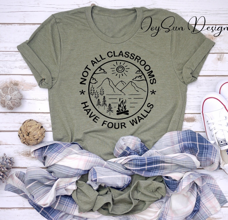 May include: A green t-shirt with a black circle graphic that says "Not all classrooms have four walls". The graphic also includes a mountain scene with a sun, clouds, trees, and a campfire.