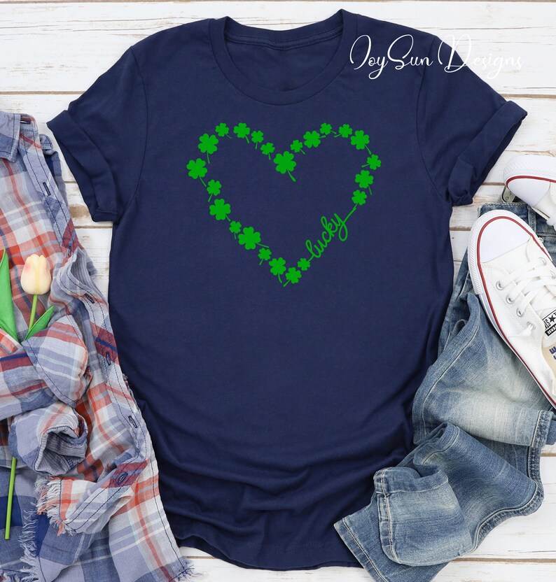 May include: A navy blue t-shirt with a green shamrock heart design and the word "lucky". This St. Patrick's Day themed shirt is a casual wear item.