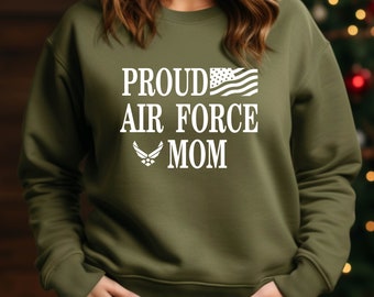 Puede incluir: Una sudadera verde con texto blanco que dice "Proud Air Force Mom" con una pequeña bandera estadounidense y el logotipo de la Fuerza Aérea.