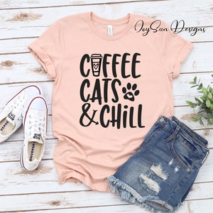 Puede incluir: Una camiseta rosa con el texto "Coffee Cats & Chill" en negro. El texto incluye una taza de caf&eacute; con un coraz&oacute;n y una huella de pata.